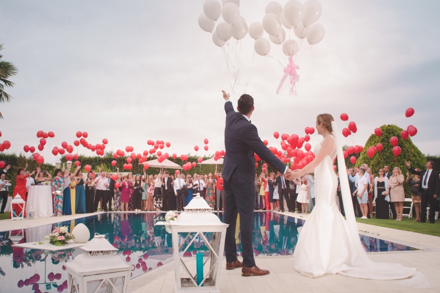 Bride and groom standing next to swimming pool and releasing white balloon bouquets into the sky