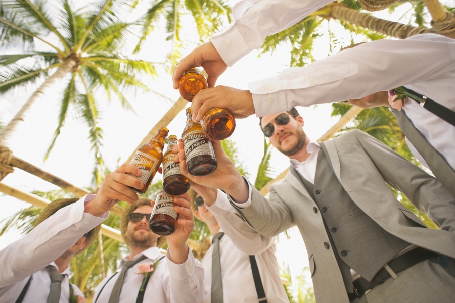 Groom and groomsmen clinking beer bottles together in celebration